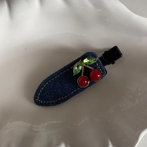 Detail of dark blue denim hair clip with red cherry beads and green crystal leaves