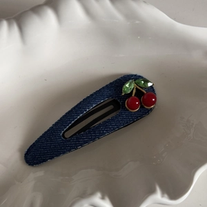 Close-up of dark blue denim hair clip with red cherry rhinestones on a shell tray