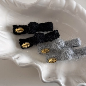 Dettaglio di fermagli per capelli in maglia soffice nera e grigia con ciondoli dorati