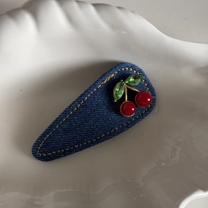 Macro view of blue denim hair clip with red cherry beads and green gemstone leaves