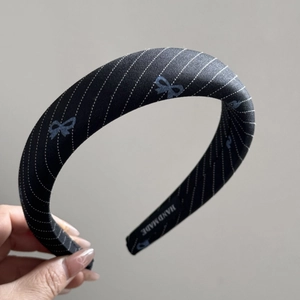 Close-up of black twill headband with blue bow print and Hand Made woven label