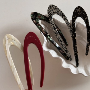 Flat lay of colorful acetate U-shaped hair pins with crystals on a white shell plate