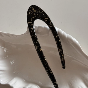 Close-up of tortoise shell pattern U-shaped acetate hair fork on a white ceramic dish