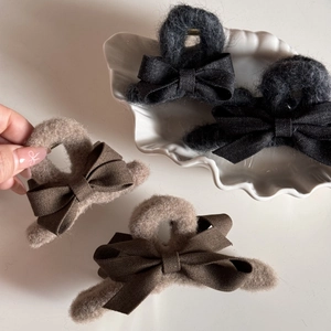 Detail of plush bow hair claw clips in black and khaki with soft faux fur texture