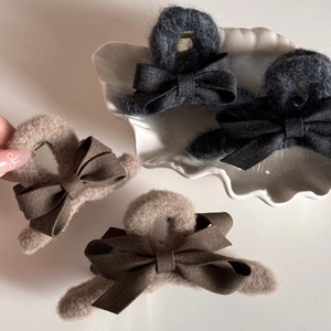 Detail view of large plush hair claws with fabric bows in dark grey and light brown tones