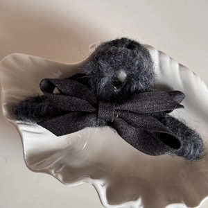 Detail view of the black plush fabric bow hair claw clip with elegant shell backdrop