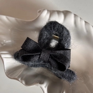 Close-up of dark grey plush hair claw clip with a black fabric bow on a shell tray
