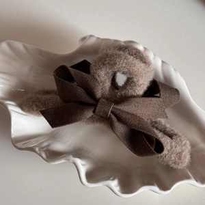 Detail shot of plush hair claw clip with brown fabric bow on a shell ceramic plate