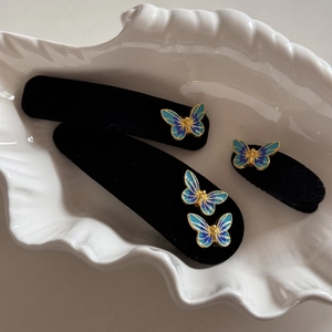 Elegant blue enamel butterfly hair clips with black velvet finish on a white tray