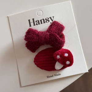 Détail d'un nœud tricoté rouge et de pinces à cheveux champignon sur carte cadeau