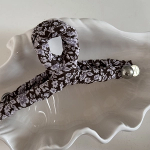 Détail de la pince à cheveux fleurie avec perle et étiquette en métal sur plateau coquillage