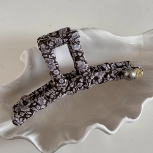 Détail d'une pince à cheveux en tissu floral avec pendentif doré et perle argentée