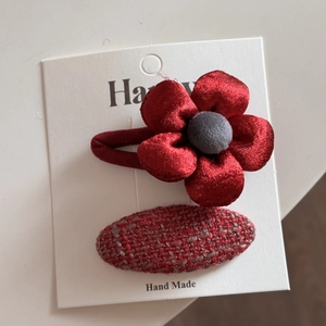 Détail d'un chouchou fleur en satin rouge et d'une pince en tweed sur carte