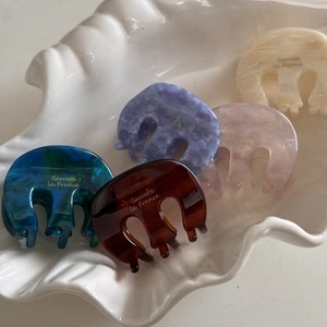 Detailed macro view of five colorful acetate hair claws on a decorative white shell tray