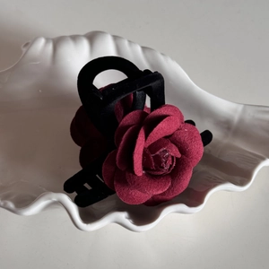 Macro shot of deep red velvet rose hair claw clip resting on a white shell tray