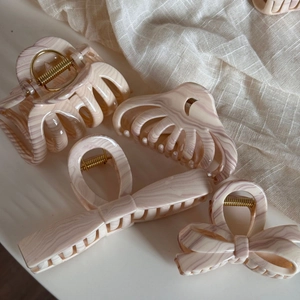 Close-up of four assorted hair claws with pink and beige marble patterns and gold springs