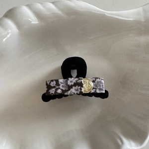 Détail de la pince à cheveux avec nœud en tissu floral, emblème doré et perle rétro