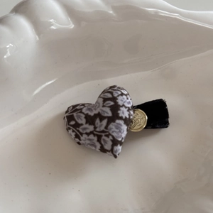 Détail d'une pince à cheveux cœur fleuri avec logo doré sur barrette en velours noir