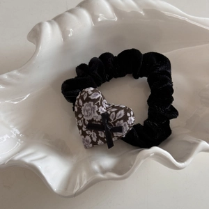 Gros plan d'un chouchou en velours noir avec pendentif cœur à fleurs et petit ruban