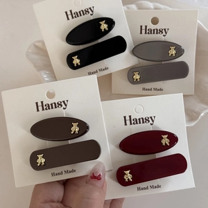 Set of four colorful hair clips featuring golden bear charms on white display card