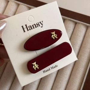 Detail of dark red resin hair clips with golden bear ornaments on a display card