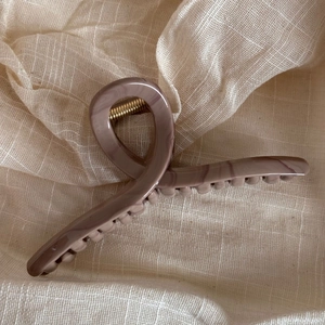 Macro shot of ripple textured marble pink hair claw clip on beige linen fabric