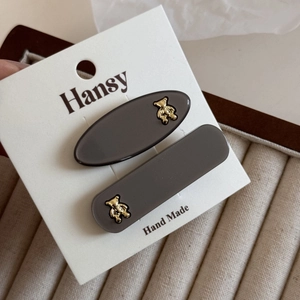 Detail of dark grey hair clips set with gold bear charms on a white display card