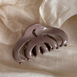 Macro detail of wave patterned mauve hair claw clip on soft beige textured linen fabric