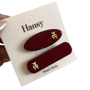 Set of two burgundy resin hair clips with golden bear ornaments on white display card