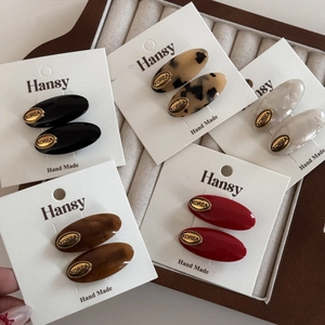 Five pairs of oval acetate hair clips in leopard, marble, and solid colors on a velvet tray