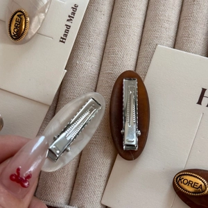 Detail of oval acetate hair clips in pearl white and amber brown with metal duckbill clips