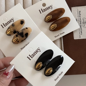 Set of oval acetate hair clips in tortoiseshell and black with gold metal emblems