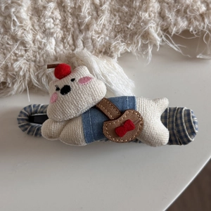 Macro detail of cute white knitted bear hair claw clip with blue fabric texture base