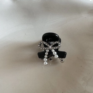 Close-up of black bow hair claw clip with rhinestones and elegant pearl pendant detail