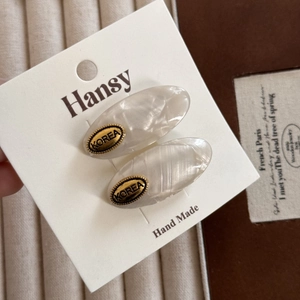 Detailed close-up of oval acetate hair clips with golden label and pearlescent texture