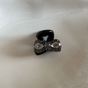 Macro detail of a black mini hair claw clip featuring a rhinestone bow design with pearls