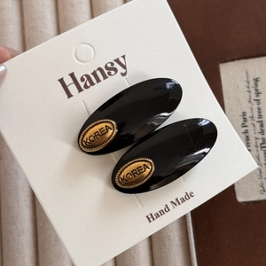 Detailed macro of black oval acetate hair clips with gold Korea metallic emblem