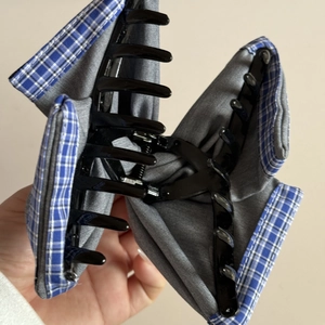 Detail of grey hair claw clip featuring blue plaid fabric and metal spring mechanism