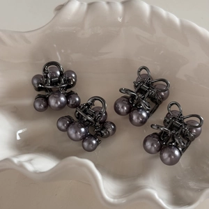 Detailed view of four mini grey cherry pearl hair claws in a white shell-shaped dish