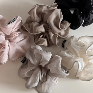 Detail view of five organza scrunchies in pastel colors with fashion labels and silver edges