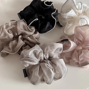 Close-up of five organza hair scrunchies in neutral tones with fashion labels and silver edges