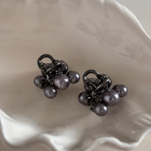 Detail view of two small dark grey pearl hair clips on a white ceramic shell tray