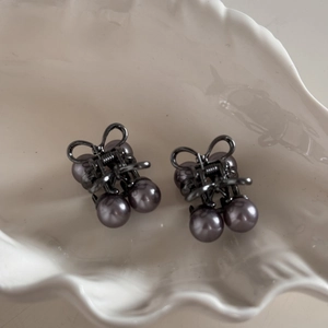 Detailed close-up of two grey pearl cherry bow hair clips in a white shell container