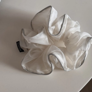 Close-up of white organza scrunchie with silver edges and a fashion brand label