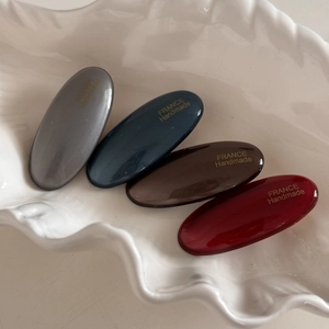 Close-up of four-piece oval hair clips in grey, navy, brown, and burgundy on a tray