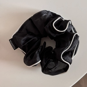 Detail of black organza scrunchie with white trim and a small fashion woven label