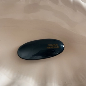 Detail of glossy black oval hair clip with gold FRANCE Handmade lettering