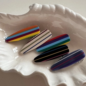 Detail view of colorful striped teardrop hair clips on a white seashell ceramic tray