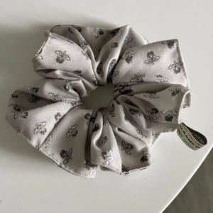 Close-up of light grey scrunchie with floral pattern and woven label details