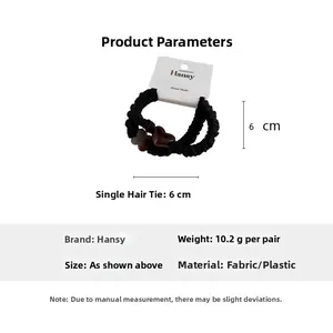 Detail of two black fabric scrunchies with resin heart and flower charms on a brand card